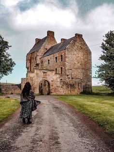 a woman walking down a dirt road in front of an old stone building on a cloudy day