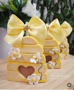 three yellow beehive shaped cookies with bows and hearts on them sitting on a table