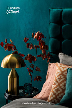 a bed with a green headboard next to a gold lamp and a blue wall