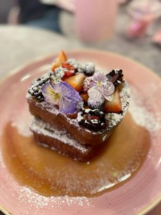 two pieces of cake on a plate covered in powdered sugar and fruit toppings