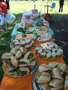 a table full of sandwiches on plates with people in the background at an outdoor event