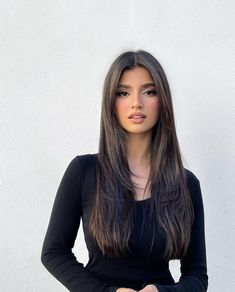 a woman with long hair standing in front of a white wall wearing a black top