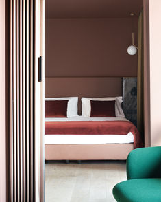 a bed sitting next to a green chair in a bedroom under a light brown wall