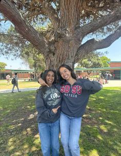 two women standing under a large tree in the grass