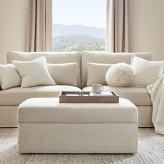 a living room with a couch, ottoman and pillows on the floor in front of a window