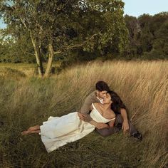 a man and woman are laying in the tall grass with their arms around each other