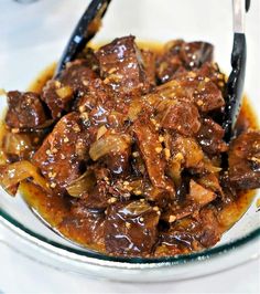 a glass bowl filled with beef and onions covered in brown sauce on top of a white table