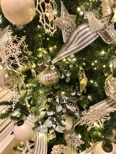 a christmas tree with ornaments and lights on it's branches is decorated in gold, silver and white