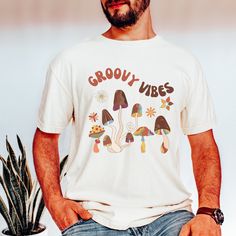 "This COZY COMFORT COLOURS t shirt with retro mushrooms and GROOVY VIBES message makes a great gif for the mushroom lover or yourself to wear casually and show off your love of fungi.  This Cottagecore, nature-inspired shirt is a great gift for nature lovers, botanists and gardeners. The unisex fit makes it great for men and women. This stylish and comfortable mushroom graphic tee is perfect for any casual occasion and makes a great gift for the mushroom lover in your life. GROOVY VIBES Mushroom shirt, aesthetic mushroom, magic mushroom, COTTAGECORE shirt,Nature lover, Fungus shirt, botanical tee *Comfort color garment dyed shirts are super popular right now and these cotton washed tees are the nicest, softest shirts to wear. The colors are true, amazing and gorgeous and will never pile. T Casual White Shirt With Mushroom Print, Cotton Short Sleeve Shirt With Mushroom Design, Graphic Tee Shirt With Mushroom Print, Summer Cotton T-shirt With Mushroom Design, Cotton Summer T-shirt With Mushroom Design, Relaxed Fit Graphic Tee With Mushroom Print, Casual Short Sleeve T-shirt With Mushroom Print, Vintage Cotton T-shirt With Mushroom Print, Casual Summer T-shirt With Mushroom Design