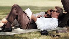 a man and woman laying on the ground next to a tree with an open book