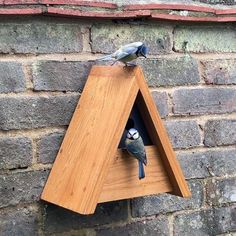 two birds perched on top of a wooden bird house in front of a brick wall