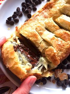 a person is holding a pastry on a plate with chocolate chips and coffee beans around it