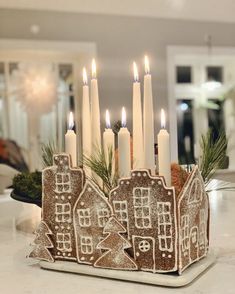 a gingerbread house candle holder with lit candles in the center, on a kitchen counter