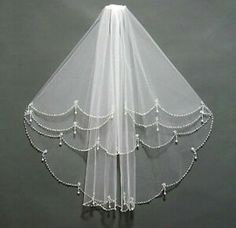 a white veil with beaded trim hanging from the ceiling in front of a gray wall