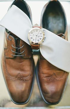 a pair of brown shoes with a white ribbon tied around them and a watch on the shoelace