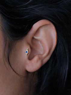 a woman's ear with a small blue diamond in the middle and a tiny white diamond on the side