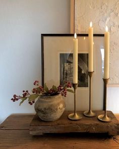 three candles are sitting on a wooden table next to a vase with flowers in it