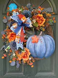 a blue pumpkin wreath with orange flowers and leaves on a green front door, next to a gray wooden door