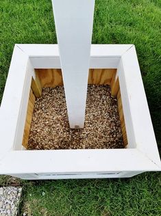 an open white box sitting on top of green grass next to a wooden pole and gravel