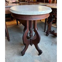 an old table with marble top and wooden legs in a room full of antique furniture