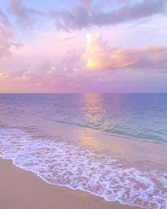 the sun is setting over the ocean with waves crashing on the beach and clouds in the sky