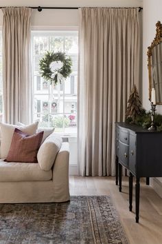 the living room is decorated in neutrals and whites, with christmas wreath on the window sill