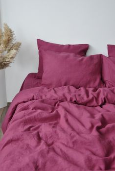 an unmade bed with pink sheets and pillows on it in a room next to a plant