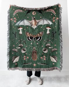 a woman holding up a green blanket with an image of bats and mushrooms on it