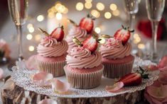 cupcakes with pink frosting and strawberries sit on a lace doily