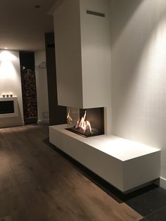 a modern fireplace in the middle of a living room with wood flooring and white walls