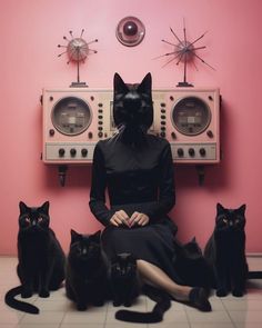 a woman sitting on the floor surrounded by black cats in front of a pink wall