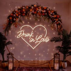 a neon sign that says drunk in love surrounded by flowers and candles on a rug