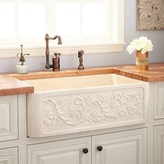 a white kitchen sink sitting under a window next to a counter top with flowers on it