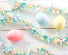 some colorful eggs and streamers on a white wooden table with blue, pink, yellow and green confetti