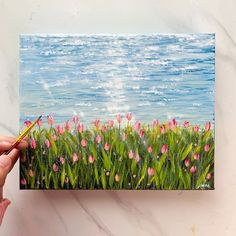 a painting of pink tulips in the grass by the ocean is being displayed