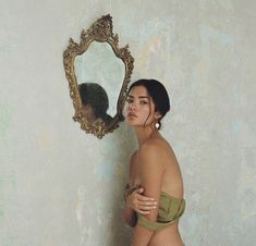 a woman standing in front of a mirror with her reflection on the wall behind her