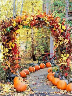 an arch with pumpkins and leaves on it in the middle of a path surrounded by trees