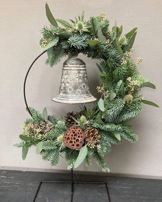 a christmas wreath with pine cones, evergreens and a bell hanging on the wall