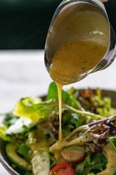 someone pouring dressing on a salad in a bowl