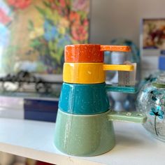 a stack of colorful cups sitting on top of a white counter next to a vase