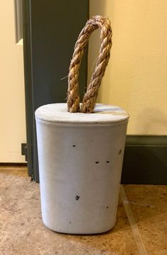 a white bucket sitting on top of a tile floor next to a door with a rope sticking out of it