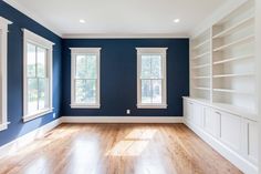 an empty living room with blue walls and white bookcases on the far wall