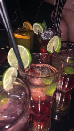 several glasses filled with different types of drinks and garnished with limes on the rim