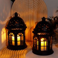 two lit lanterns sitting next to each other on top of a white tablecloth covered floor