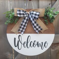 a welcome sign hanging on the side of a wooden fence with burlocks and greenery