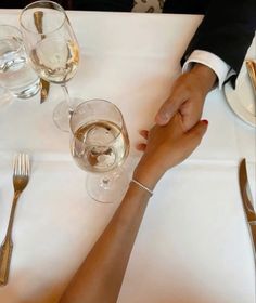 two people holding hands at a table with wine glasses and silverware on top of it