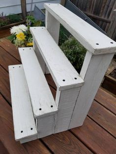 two white wooden benches sitting on top of a wooden deck next to flowers and potted plants