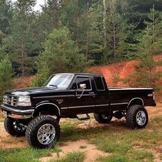 a black pickup truck parked on top of a dirt road in front of some trees