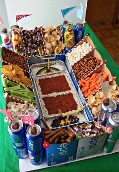 a football snack stadium is displayed with snacks and dips on the table, along with beer cans