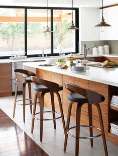 a kitchen island with three stools in front of it and an open window to the outside